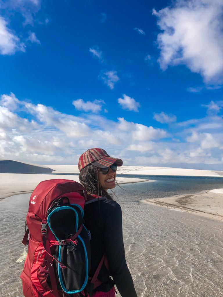 Ana nos Lençóis Maranhenses de mochila cargueira vermelha, sorrindo em frente às lagoas azuis