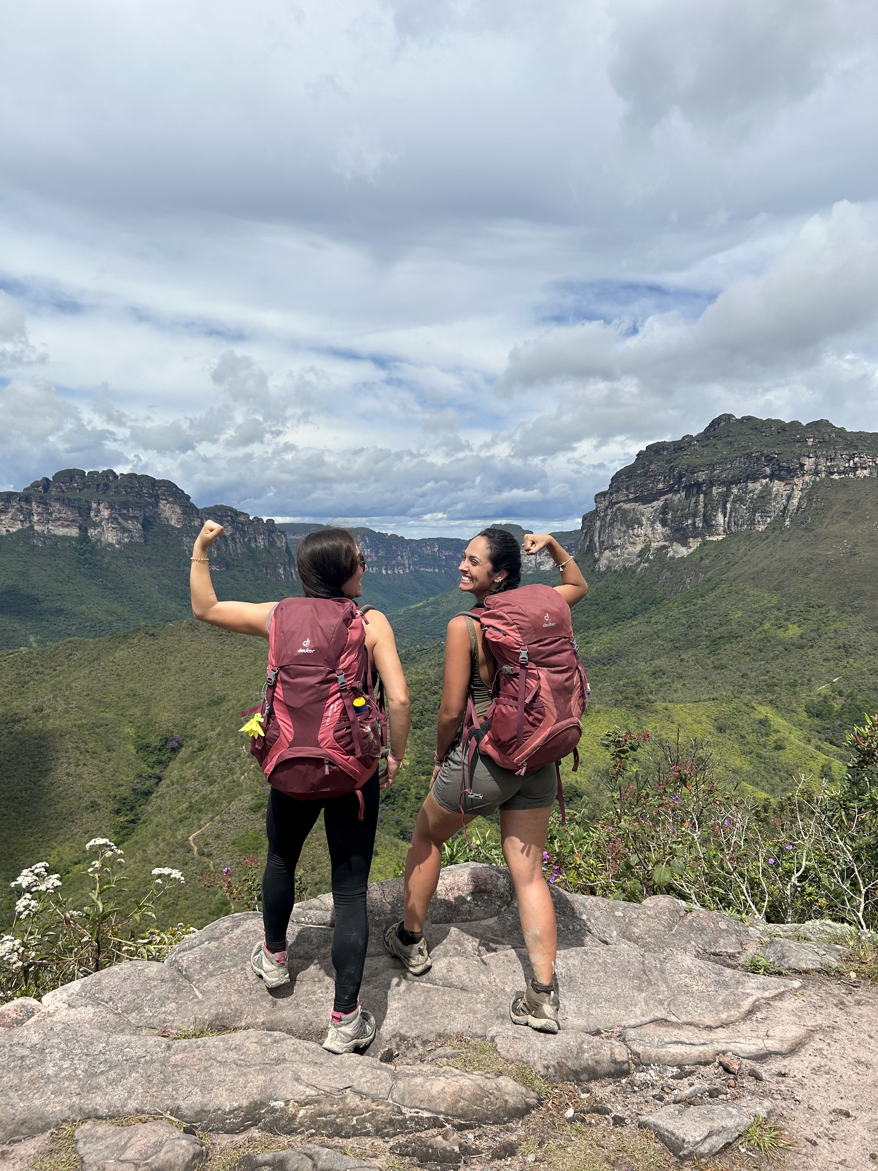 Duas viajantes de costas com mochilas cargueiras vermelhas fazendo pose forte no mirante da Chapada Diamantina